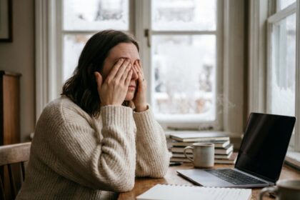 Blogueuse fatiguée qui se frotte les yeux devant son ordinateur portable en hiver dans un bureau à domicile chaleureux